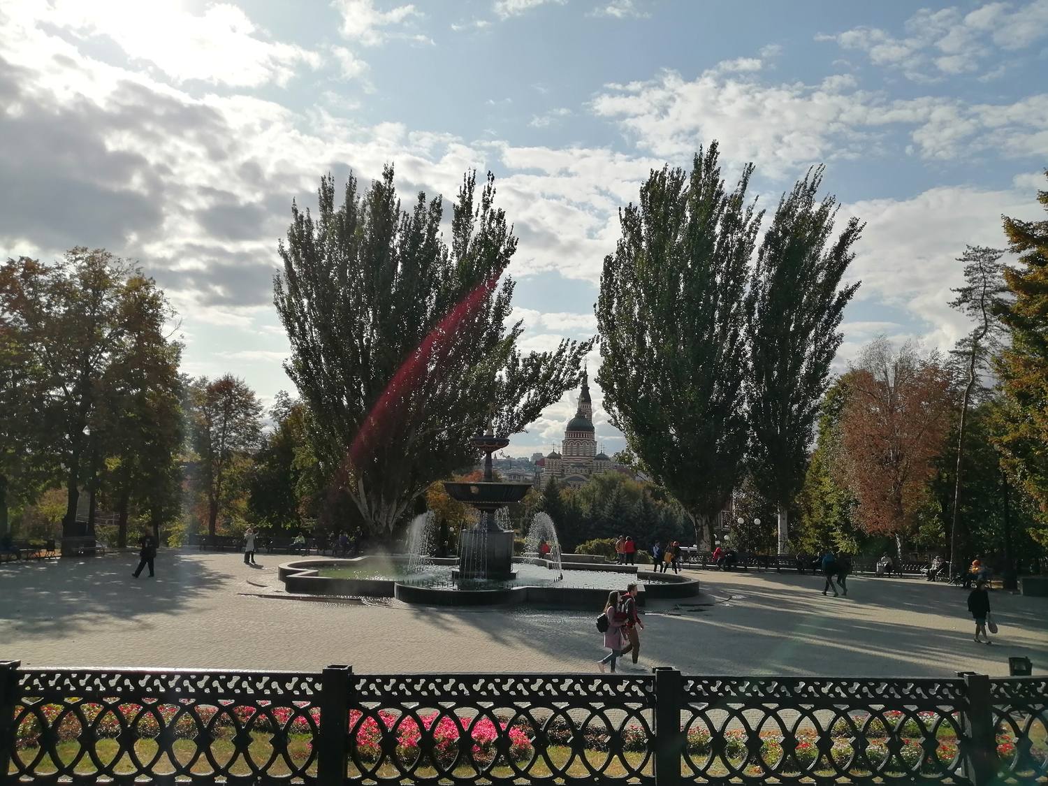 A fountain in Shevchenko Garden in Kharkiv with a cathedral dome beyond the trees